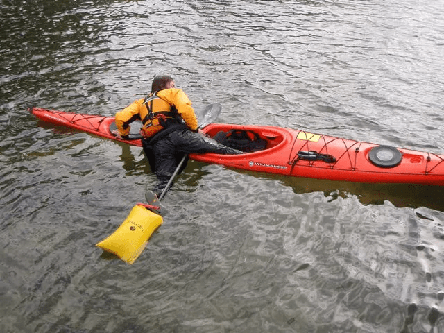 A man using his paddle float to get back in his kayak after capsizing