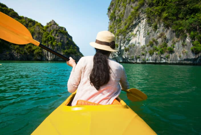 A woman kayaking in summer with a hat and light, long-sleeve shirt